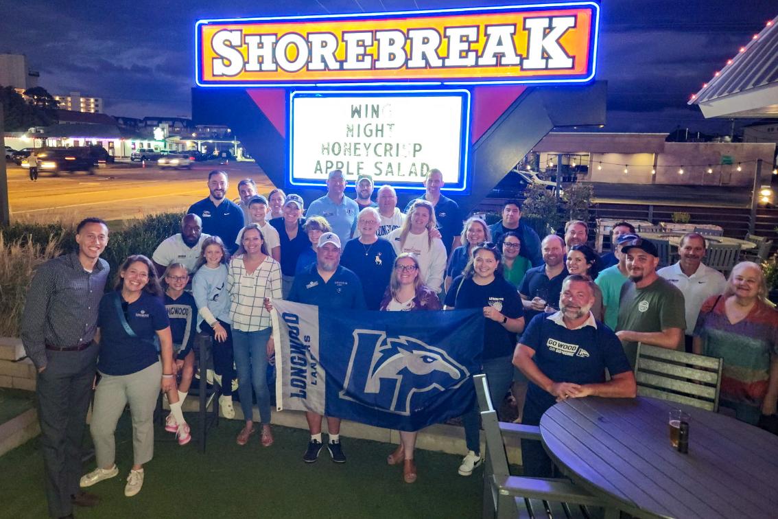 Longwood alumni and families gather at a 757 regional event while holding a Longwood Lancers flag.