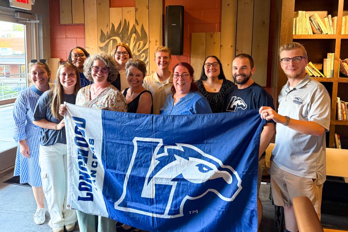 Longwood alumni and families gather at a Blue Ridge regional event while holding a Longwood Lancers flag.