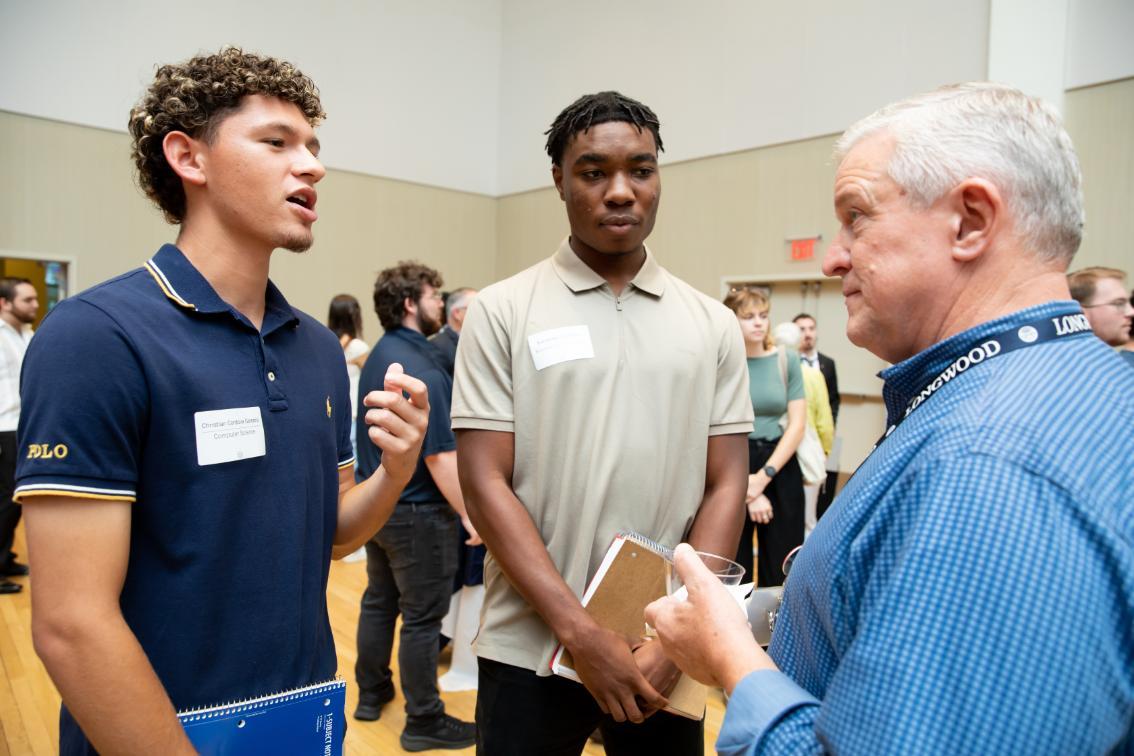 Two students and an alum chatting at a networking event
