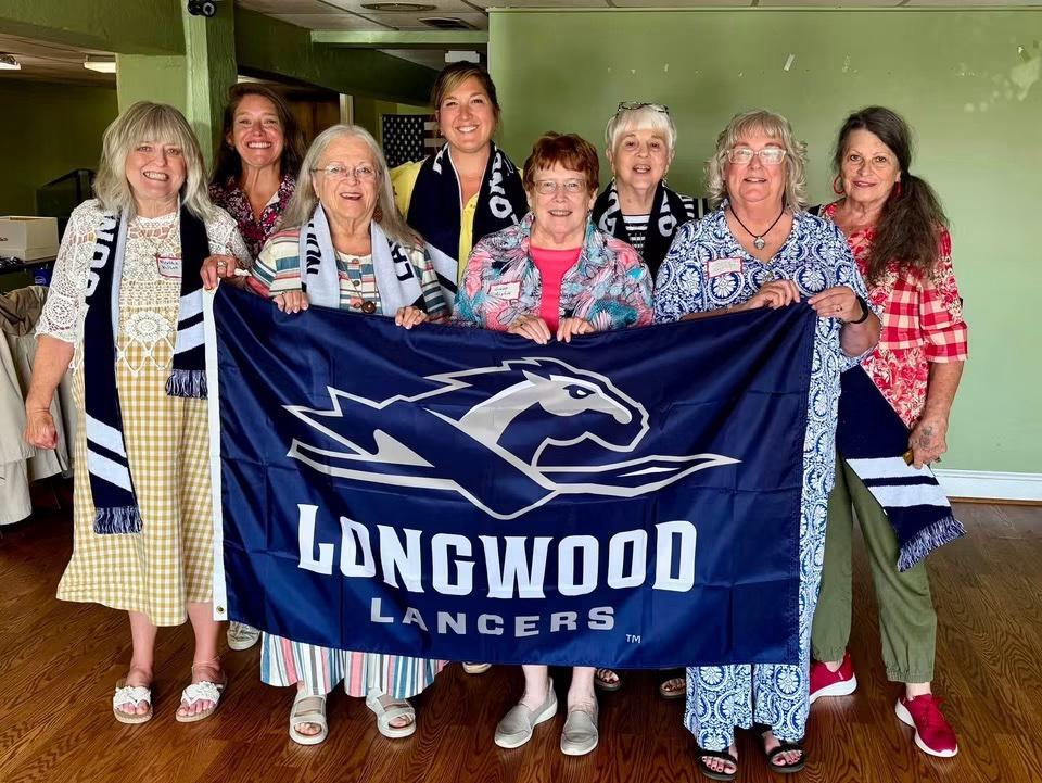 Longwood alumni and families gather at a MHC regional event while holding a Longwood Lancers flag.