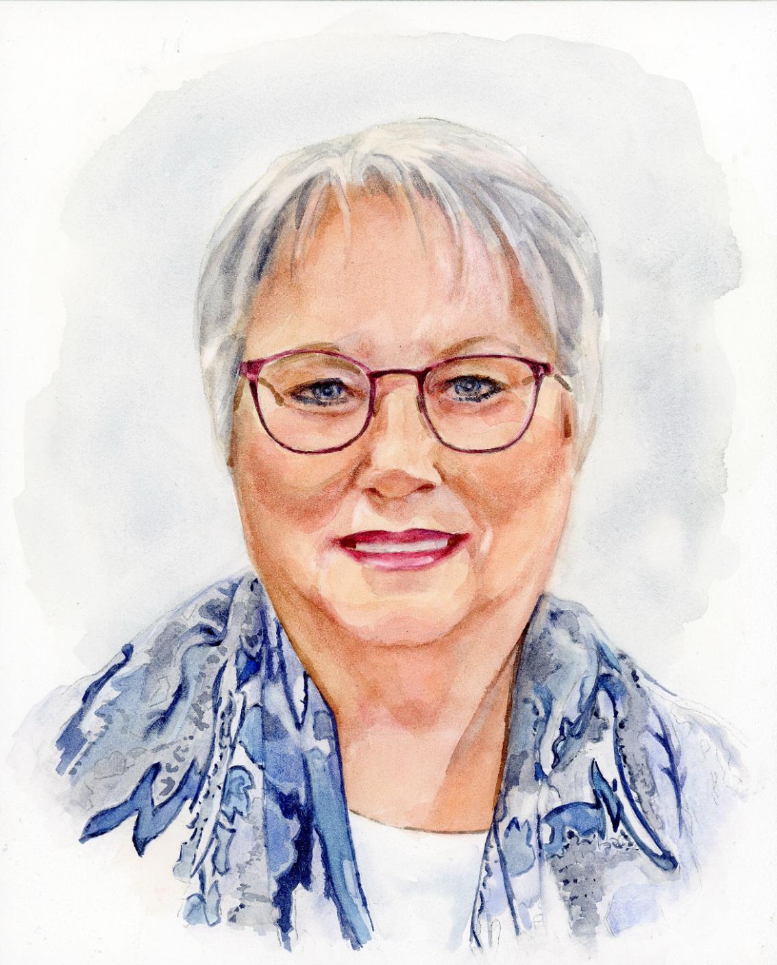 Watercolor portrait of Karen Mitchell Schinabeck, smiling and wearing glasses, a white top, and a blue patterned scarf. The background is a soft watercolor wash.