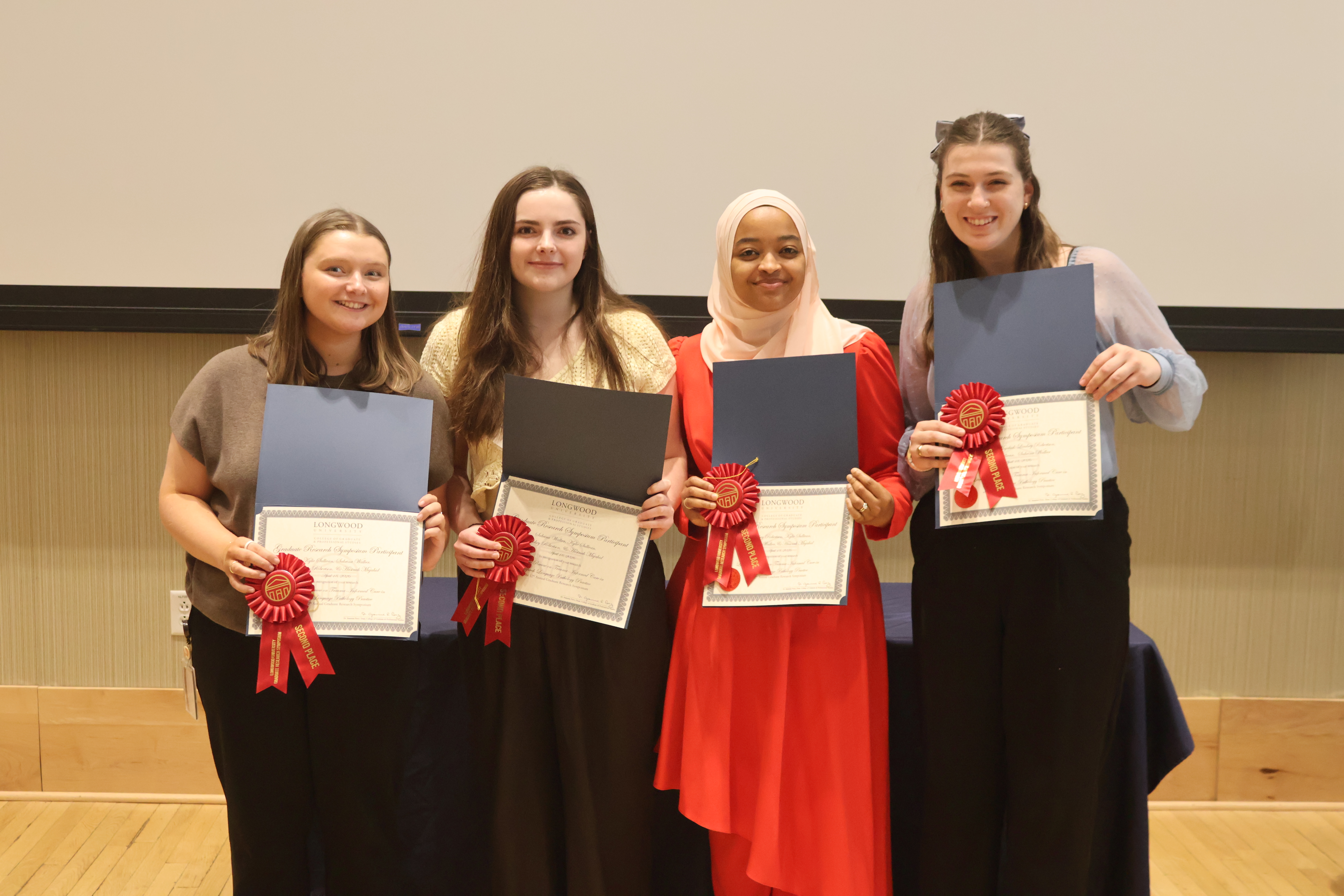 - Four Longwood graduates smile while holding certificates and second-place award ribbons.