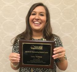 Lucy Wallace, Outstanding Student Leader Award - A person holds a plaque recognizing student leadership in SHAV.   The award is titled “SHAV Outstanding Student Leader 2019.”   It was presented to Lucy Wallace for notable contributions.   The background shows a patterned wall in an indoor setting.