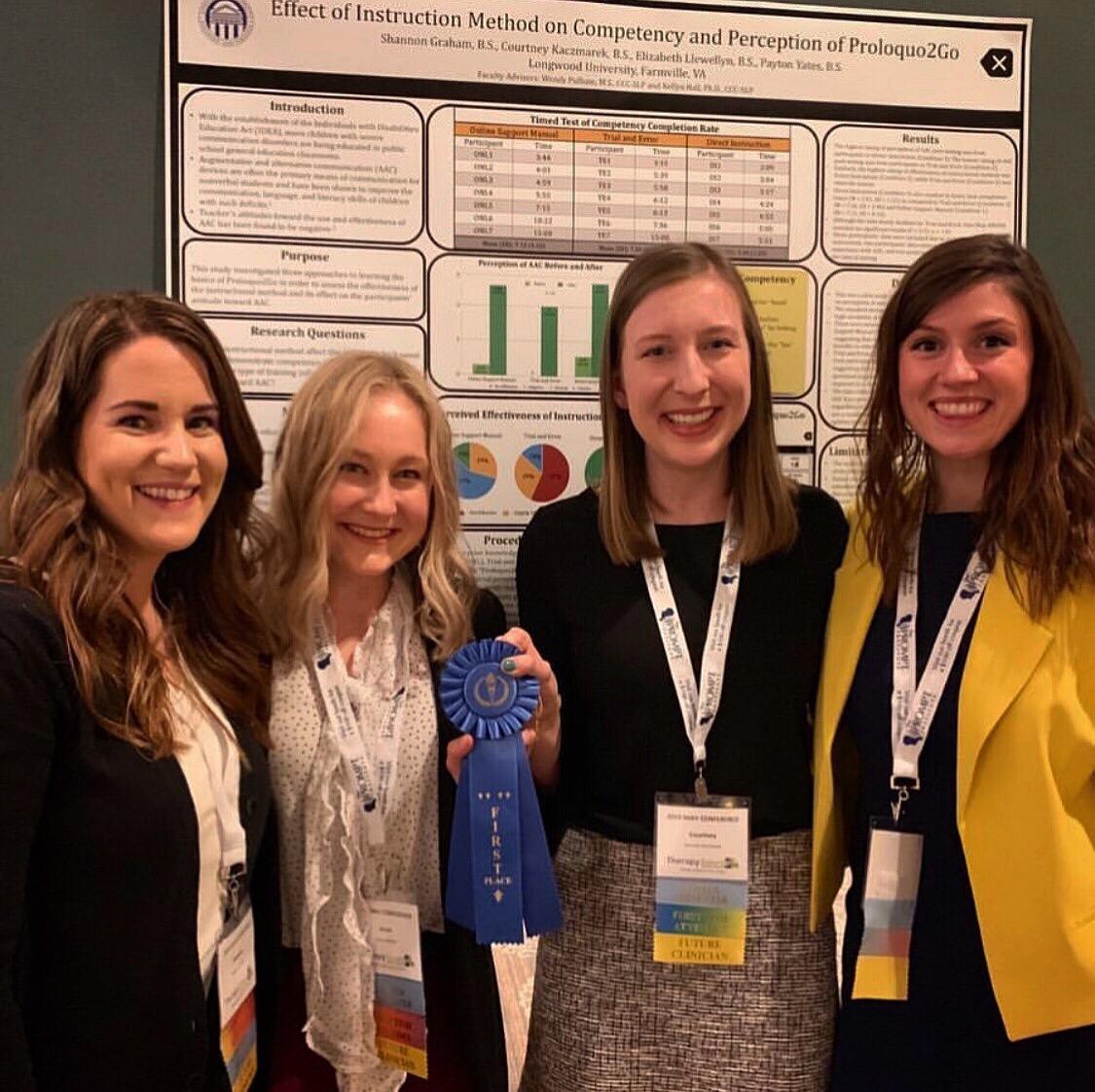 - Four women stand smiling in front of a research poster. One holds a blue first-place ribbon toward the camera. They wear conference badges and professional attire. Charts, graphs, and text from their project fill the poster behind them.