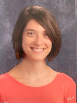 Headshot of Rachael O’Donnell - A woman with a short brown bob smiles warmly in a studio-style portrait. She wears a coral-colored top against a mottled gray background. Her expression is friendly, and the lighting is soft and even.