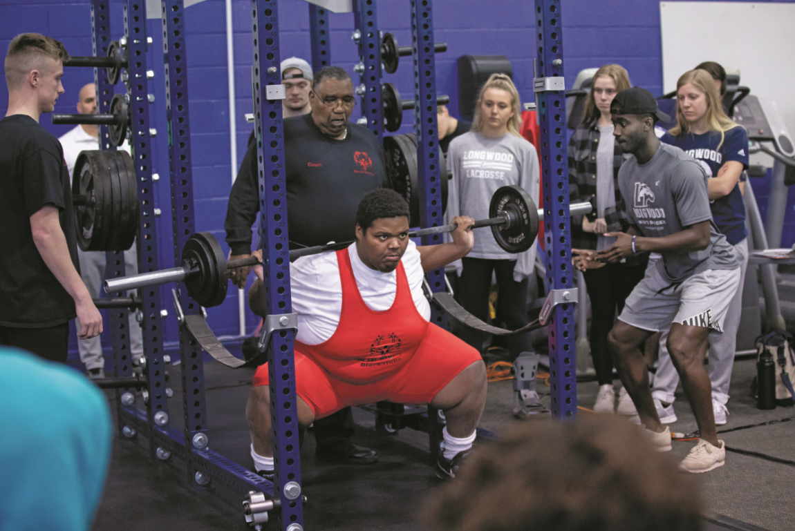 Willy Miezan ’19 (right, wearing cap), who volunteered to be a spotter during the event, encourages a lifter to do his best.