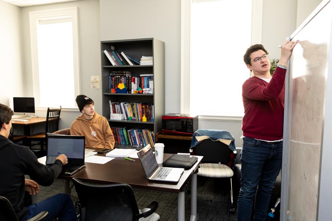Longwood University students working through a problem together at a whiteboard