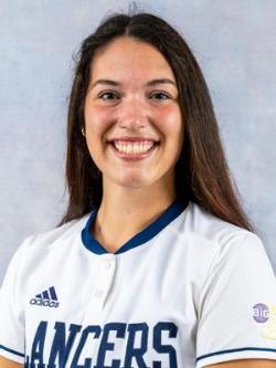 - A Longwood University softball player poses for a team headshot. She wears a white Lancers jersey with an Adidas logo and Big South patch. The student-athlete smiles toward the camera against a neutral studio background. Her long dark hair is worn down.