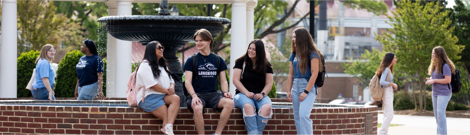 Students gather and talk around a campus fountain on a sunny day at Longwood University.