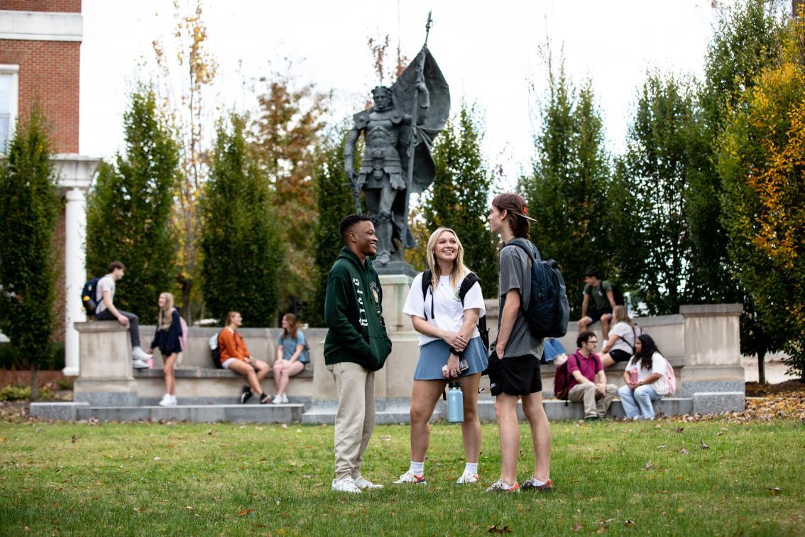 Students gather on the lawn and around the base of the Joan of Arc statue located at the south end of campus