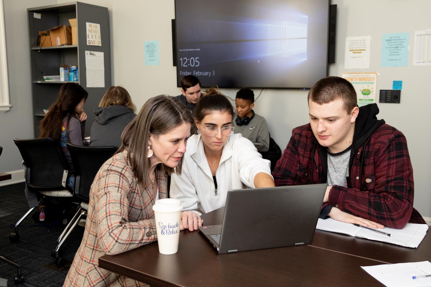 Students and a faculty member work together around a laptop in the Quantitative Reasoning Center, with other students collaborating in the background.